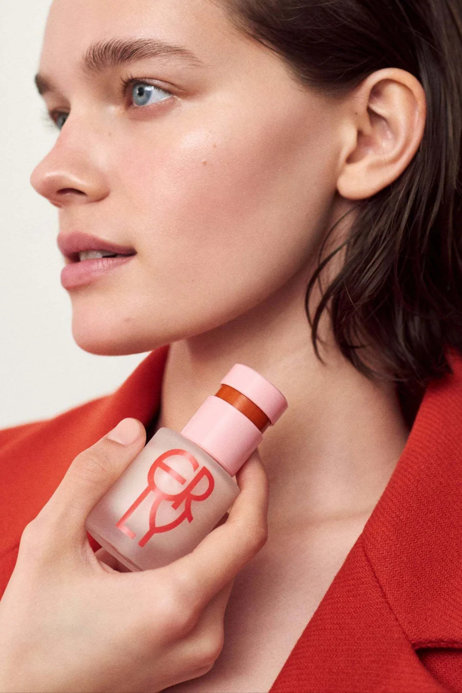 Woman holding a pink bottle with a logo, wearing a red jacket.